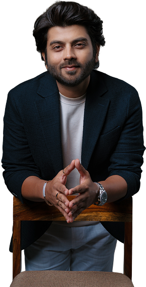 Jay Thadeshwar leaning on a chair with hands clasped, dressed in a blazer and casual attire, exuding confidence.